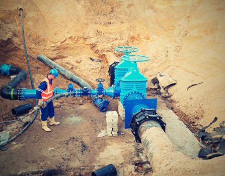 Worker works underground for reconstrucion of drink water system. Technical expert at  gate valve on new pipeline system check of repaired connection before covering by clay
