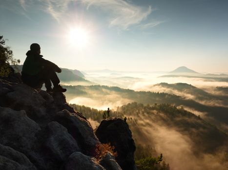 Hiker man take a rest on mountain peak. Man lay on summit, bellow autumn valley. Bright morning Sun shining in sky. 