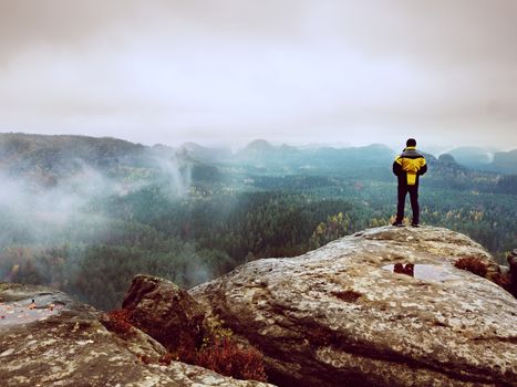 Rear view of male hiker in yellow black jacket on rocky peak while enjoying a daybreak above mountains valley 