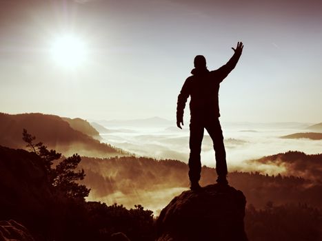 Happy man with raised arms gesture triumph  on exposed cliff. Satisfy hiker silhouette on sandstone cliff watching down to hilly  landscape. 