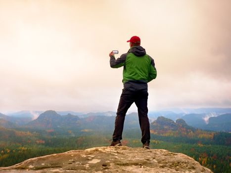 Man photography with phone of dreamy hilly landscape, spring orange pink misty sunrise in a beautiful valley of rocky mfountains.