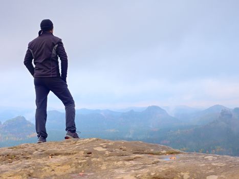 Foggy rocks. Hiker kin black on sharp cliff of sandstone rock in rock empires park and watching over misty and foggy spring valley