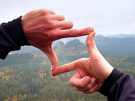 Close up  hands make frame gesture. Melancholy misty valley bellow rocky peak. Cold spring daybreak in mountains.