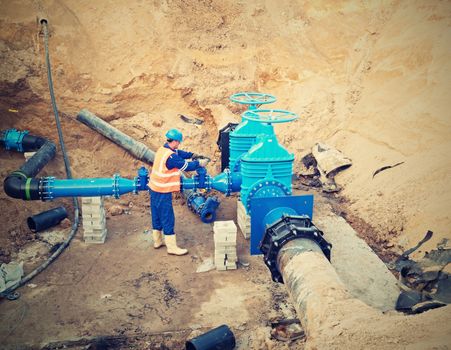Worker works underground for reconstrucion of drink water system. Technical expert at  gate valve on new pipeline system check of repaired connection before covering by clay