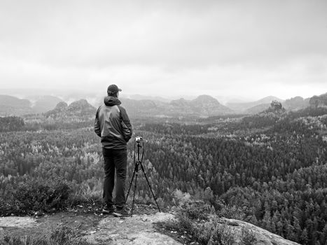 Nature photographer stay at tripod with mirror camera on peak of rock. Dreamy fogy landscape, spring orange pink mist