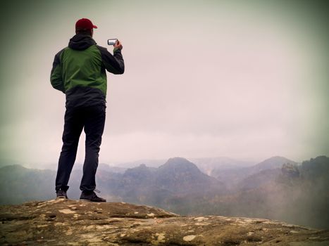 Man photography by phone. Trip in rocky mountains, sharp rock empire. Misty spring landscape, gentle mist
