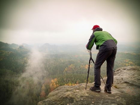 Nature photographer stay at tripod with mirror camera on peak of rock. Dreamy fogy landscape, spring orange pink mist