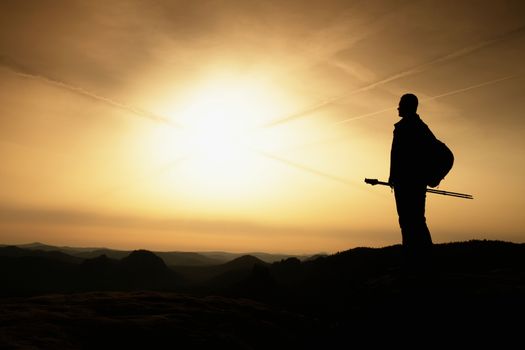 Sunny fall morning. Hiker is standing on the peak of rock in rock empires park and watching over autumn misty and foggy morning valley to Sun.  Soft focus.