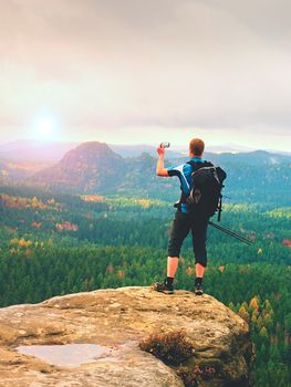 Man takes photos with smart phone on peak of rock empire. Dreamy colorful nature with autumnal orange pink mist in a beautiful valley of rocky mountains.