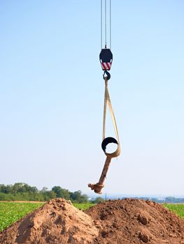 Hanging old tube on crane rope. Clear blue sky in background