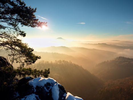 Freeze daybreak, rocks covered with fresh powder snow. Stony rock peak above foggy valley. Winter misty sunrise in a beautiful rocks empire. 