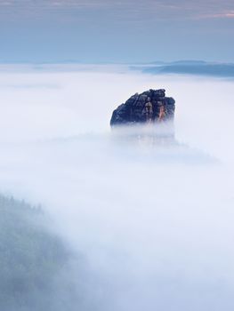 Sharp sandstone rock empire sticking out from heavy fog. Deep misty valley full of creamy mist. Popular climbers resort in autumn look