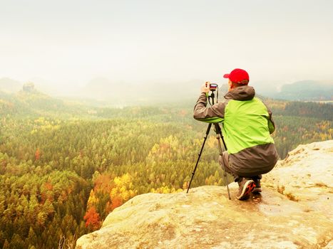 Nature photographer sit on rocky edge and takes photos with mirror camera on peak of rock.