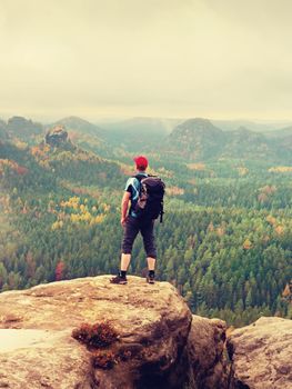 Alone tourist with outdoor sportswear and backpack stand on cliff edge  and watching into colorful autumn valley bellow.  Vintage Style Toned effect