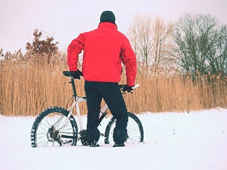 Sportsman with mountain bike lost in snow. Lost path  in deep snowdrift.  Snow flakes melting on dark off road tyre.  Winter weather in the field.