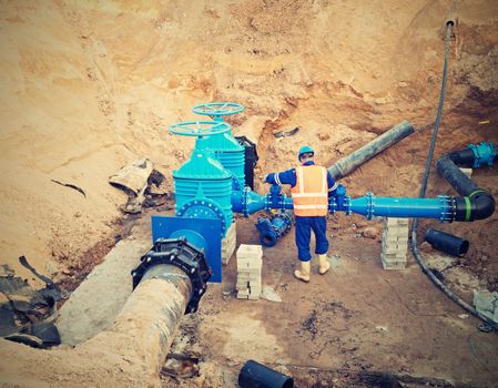 Worker works underground for reconstrucion of drink water system. Technical expert at  gate valve on new pipeline system check of repaired connection before covering by clay