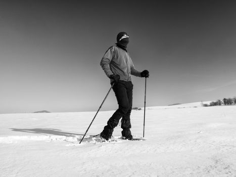 Tourist with snowshoes walk in snowy drift. Sunny freeze weather. Hiker in pink sports jacket and black trekking trousers snowshoeing in powder snow.