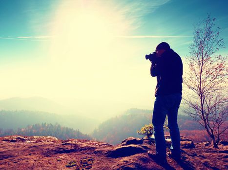 Tall  man is taking photo by mirror camera on neck. Snowy rocky peak of mountain. Professional photographer takes photos with mirror camera on peak of snowy rock. 