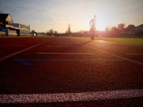 Sportsman on red running stadium racetrack. Adult man in evening training at sunset. Sport and healthy lifestyle concept and jogging civic training workout