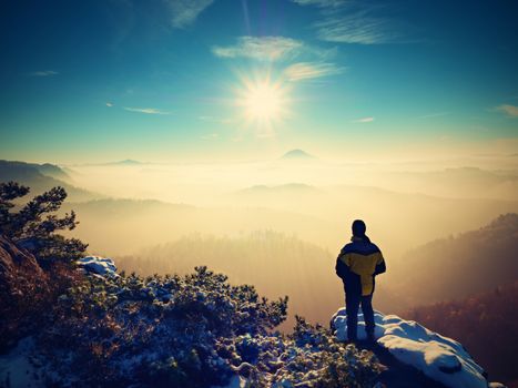 Tall hiker in black on rocky peak watch the world . Heavy orange mist bellow in valley. Wonderful breathtaking daybreak in mountains.