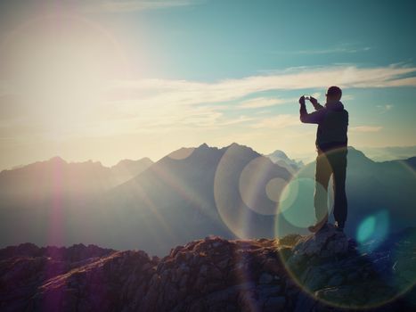 Lens flare light, strong effect. Bow light circles.  Hiker takes selfie photo. Tourist at mountain peak. Daybreak horizon above blue foggy valley. Mountains increased from humidity