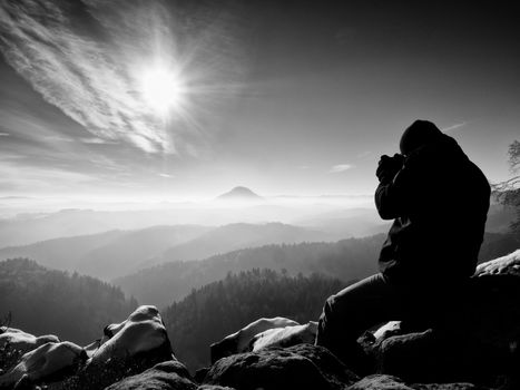 Tall  man is taking photo by mirror camera on neck. Snowy rocky peak of mountain. Professional photographer takes photos with mirror camera on peak of snowy rock. 