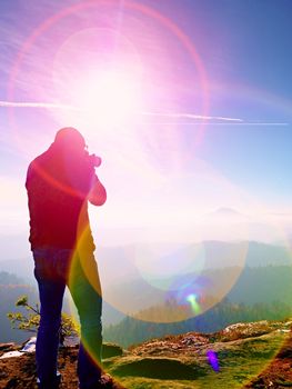 Tall  man is taking photo by mirror camera on neck. Snowy rocky peak of mountain. Professional photographer takes photos with mirror camera on peak of snowy rock. 