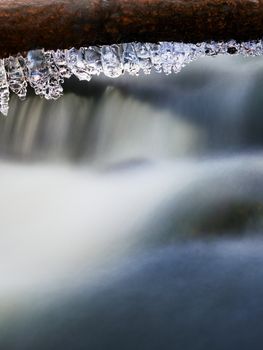 Icicles hang on twigs and icy bark above chilli rapid stream. Winter mountain stream, long thin icicles are hanging on fallen trunk.