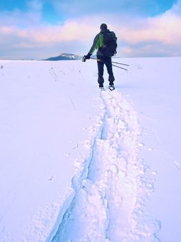 Hiker with backpack snowshoeing  in deep drift. Man with snowshoes walk in hill. Hiker in green gray winter jacket and black trekking trousers snowshoeing in powder snow.