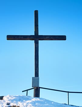 Sharp summit  with modest cross raised  on mountain peak. Winter daybreak Sun in sky. Wooden unpretentious crucifix in memory of victims of mountains. Vivid photo.