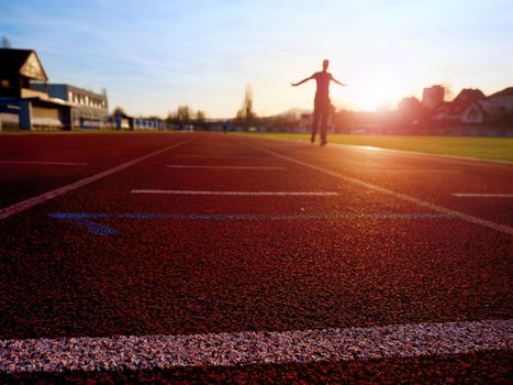 Sportsman on red running stadium racetrack. Adult man in evening training at sunset. Sport and healthy lifestyle concept and jogging civic training workout