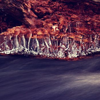 Close up view of structured ice above a motion blur water stream. Creative long exposure winter photography. 
