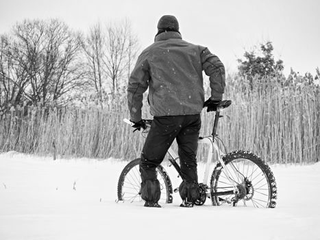 Sportsman with mountain bike lost in snow. Lost path  in deep snowdrift.  Snow flakes melting on dark off road tyre.  Winter weather in the field.