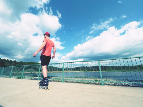 Roller skater in action. Man ride in inline skates ride along promenade handrail, blue sky in background. Low angle view