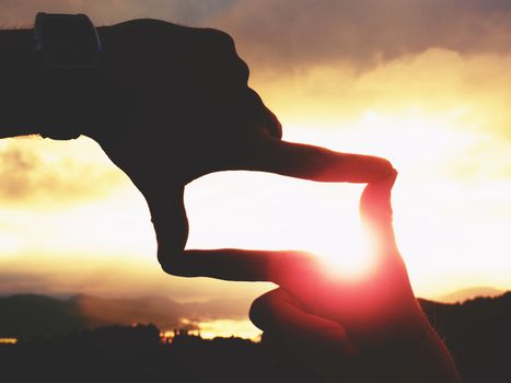 Close up of hands with watch making frame gesture. Dark misty valley bellow in landscape. Sunny autumn daybreak in mountains.