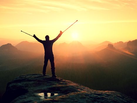 Happy man with broken leg and medicine crutch.  Hiker with leg in immobilizer achieve peak of mountain. Daybreak misty valley bellow silhouette. 