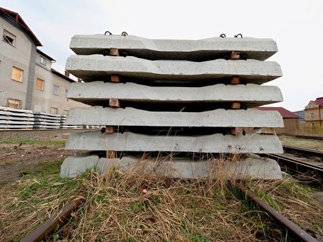 Sleepers stock in railway depot. New concrete railway ties stored for reconstruction of old railway station. Old houses  in background