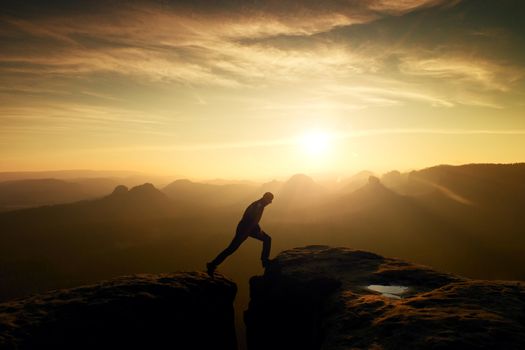 Jumping man. Young man makes jump on colorful sky background in mountains. heavy orange mist in deep valley. Miracle of nature