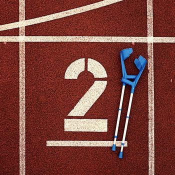 Medicine crutch for broken leg. Number two. Big white track number two on red rubber racetrack. Gentle textured running racetracks in athletic stadium.