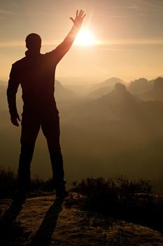 Man takes photos with phone on rock empire. Dreamy fogy mountains, spring orange pink misty sunrise in a beautiful valley of rocky mountains.