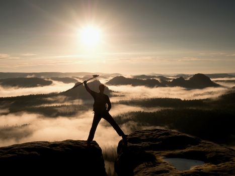 Hiker on peak. Tourist with bag in target with trekking poles in hand raised in air. Marvelous daybreak in fogy mountains