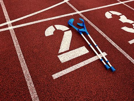 Medicine crutch for broken leg. Number two. Big white track number two on red rubber racetrack. Gentle textured running racetracks in athletic stadium