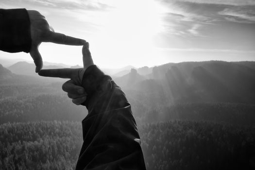 Female hands do frame gesture. Deep misty valley bellow sandsotne cliff.  Sunny spring daybreak in rocky mountains. Black and white photo