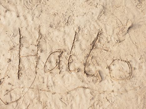 Children drawing of word hallo in sand on beach of bay. Letters written in wet muddy sand. 