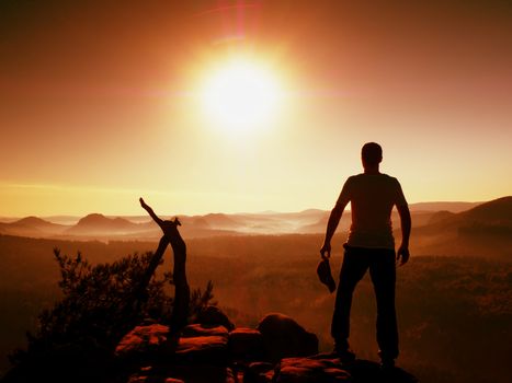 Hiker in grey t-shirt with red  cap in hand stay on rocky peak. Man watching over  valley to Sun. Beautiful moment the miracle of nature. Vintage effect. 