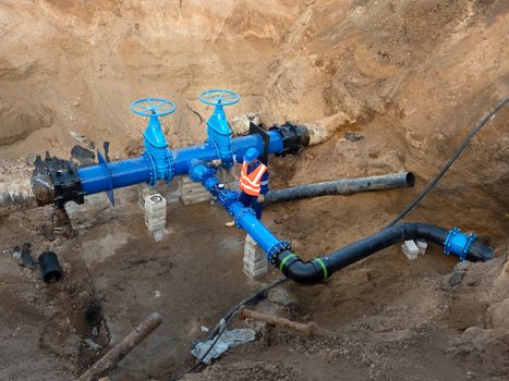 Technical expert open gate valve on 500mm drink water pipes joined with new black waga multi joint members into old pipeline system. Man control  finished repaired piping before covering by clay. Asphalt isolation. 