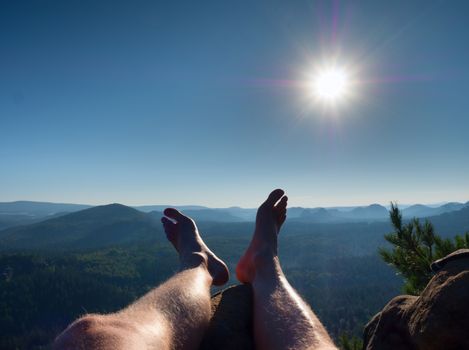 Naked male hairy legs take a rest on peak of rock. Outdoor activities in summer weather. Long forest valley in hilly landscae of nature park.