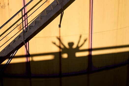 People shadows on old metal tanks in power plant, old kind of factory plant. Metal construction with old yellow paint and rusty places. Iron circle ladders around construction
