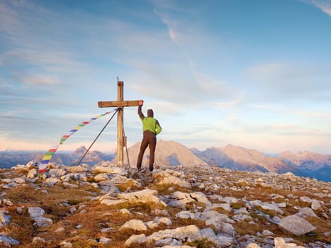 Tourist stand on rocky view point and watching into misty Alpine valley. Wooden cross at a mountain peak. Cross on top of a mountain peak as typical in the Alps. 