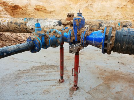 Old big drink water pipes joined with new blue gate valves and reduction joint members. Finished repaired piping waiting for covering by clay. Extreme kind of corrosion, metal corroded texture.